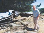 Leader Valley farmer Andrew Harris with a haybarn destroyed by the November 14 quake. Its eight supporting timber poles all snapped cleanly off at ground level.